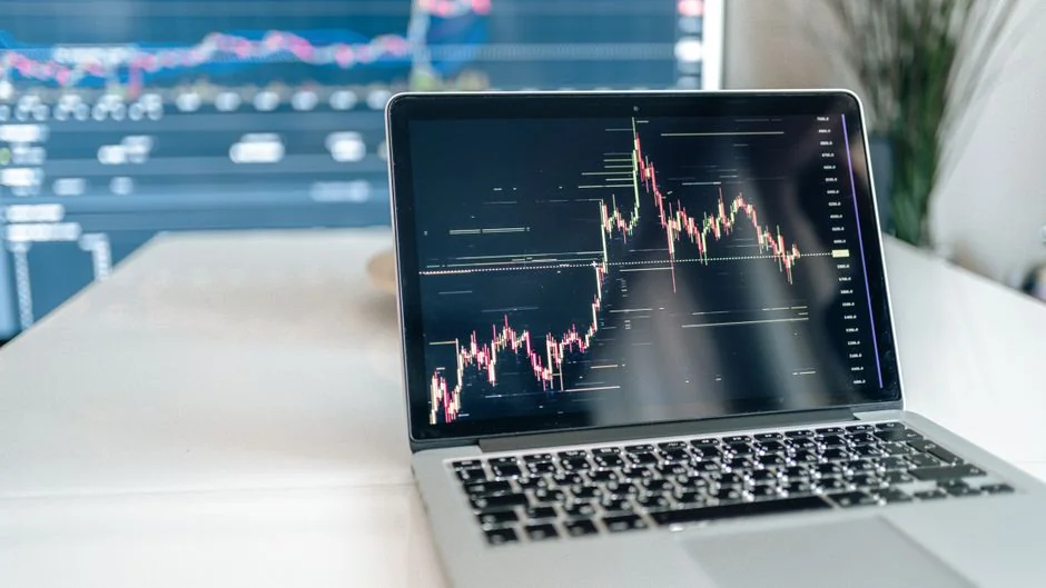 Two businessmen analyze stock market data using a smartphone and laptop in a modern office setting.